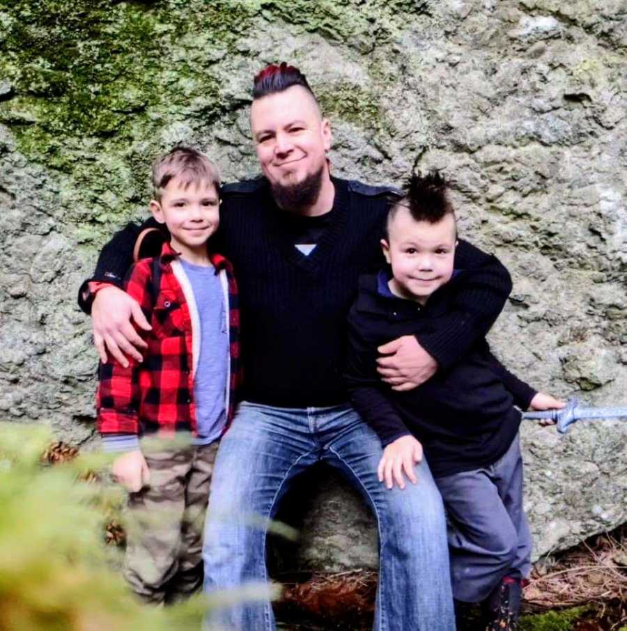 Dad with a red and black mohawk hugs his two sons for a photo while hiking