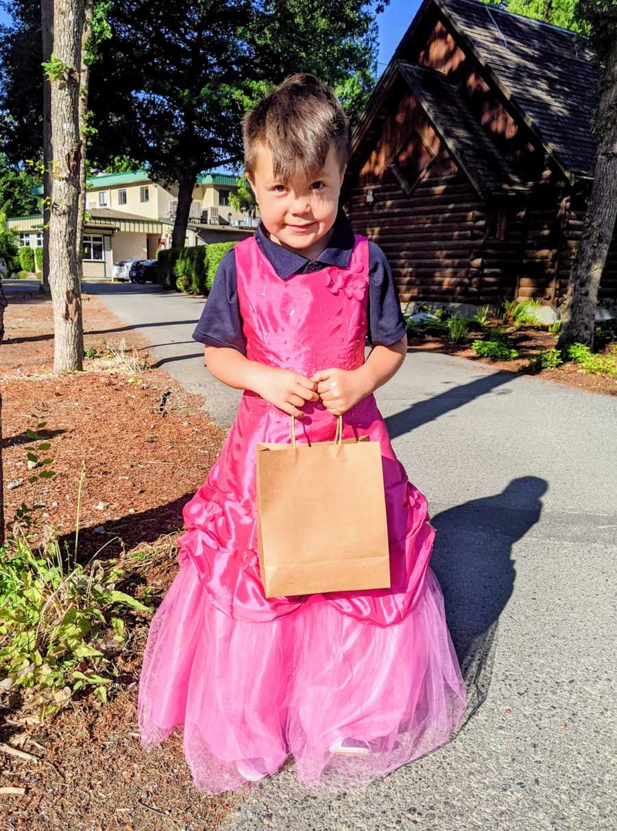 Little boy smiles shyly while wearing a hot pink princess dress