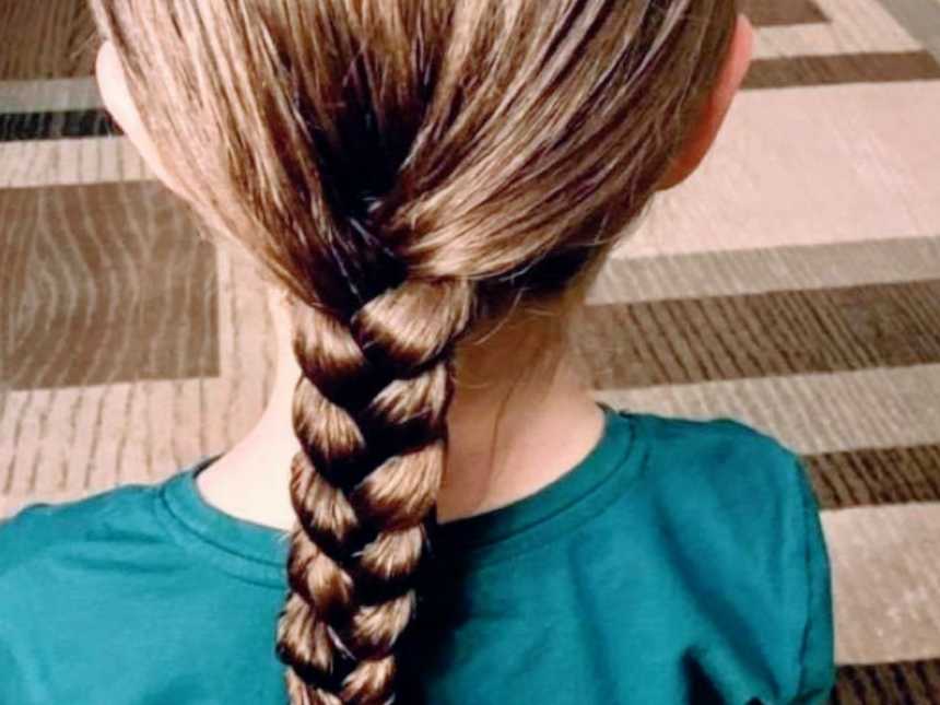 Little girl sits on the floor and shows off her freshly braided hair