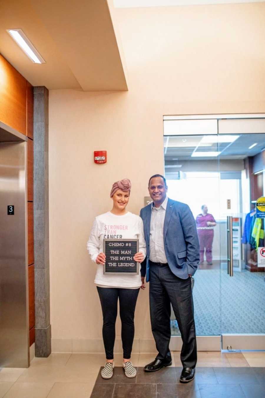 Woman with triple negative breast cancer takes a photo with her doctor with a sign that reads "the man, the myth, the legend"