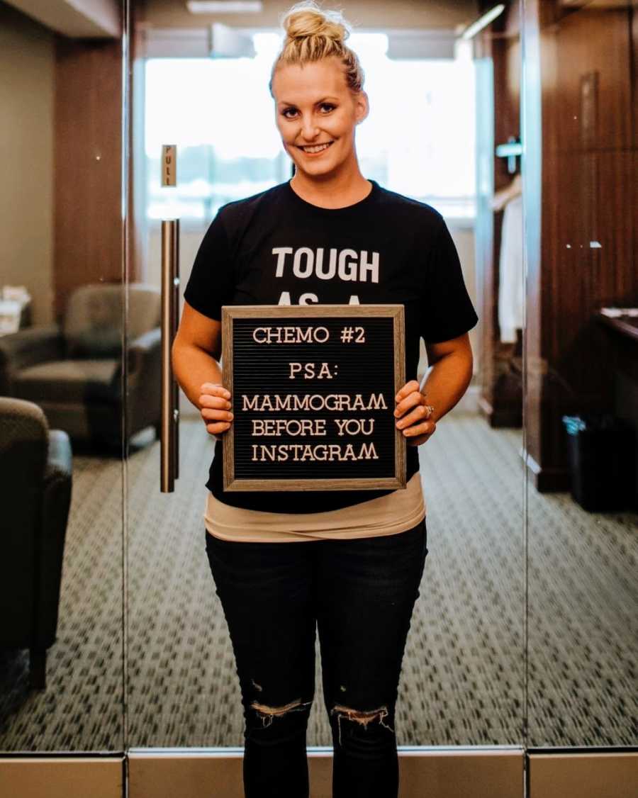 Young woman diagnosed with breast cancer takes a picture with a sign that says "PSA: Mammogram before you Instagram"