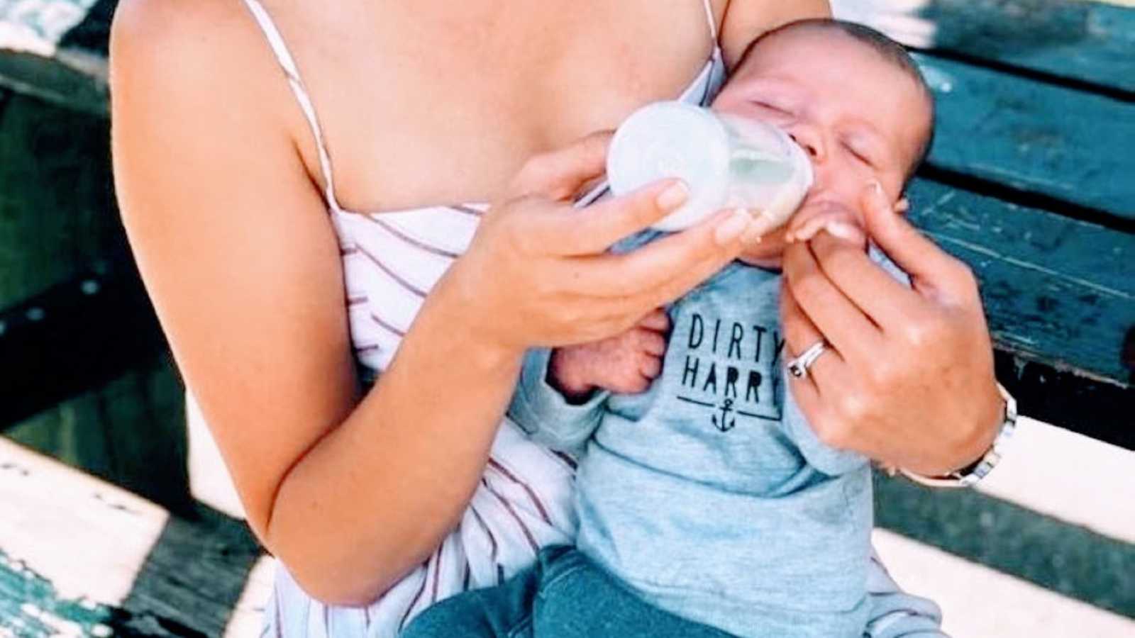 Newborn son peacefully bottle feeds while at a park