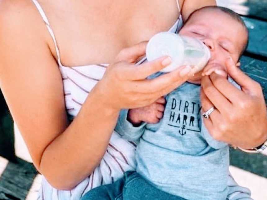 Newborn son peacefully bottle feeds while at a park