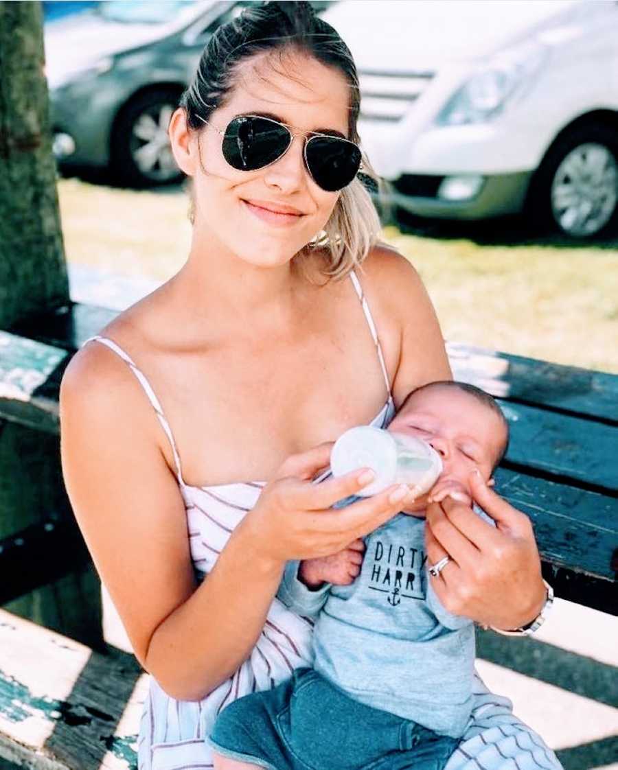 Young mom proudly bottle feeds her son while they sit out at a breezy park