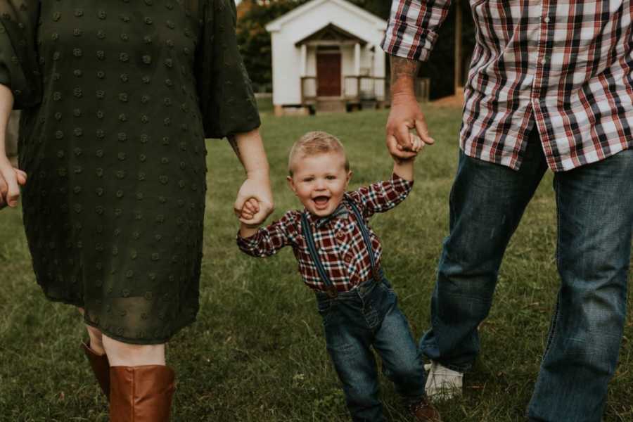 Parents take a photo with their son skipping and smiling and holding their hands after adopting him