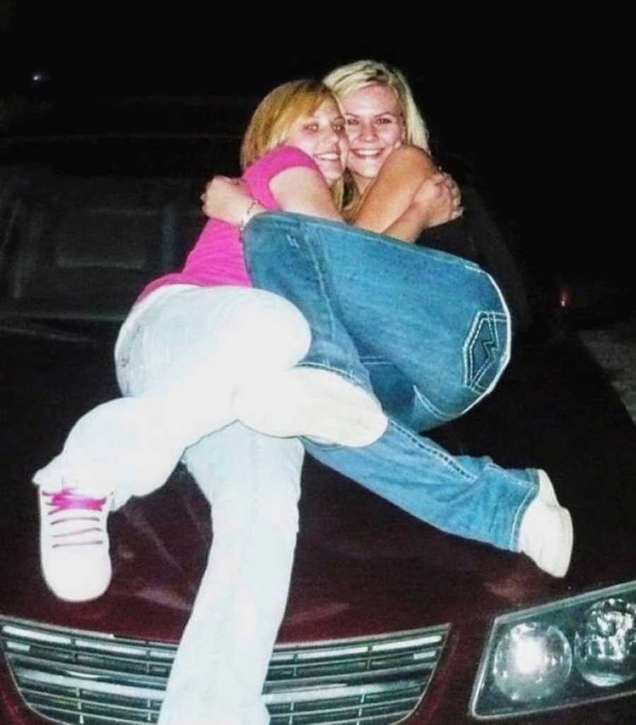 High school girls take a photo together hugging each other while sitting on top of a car at night