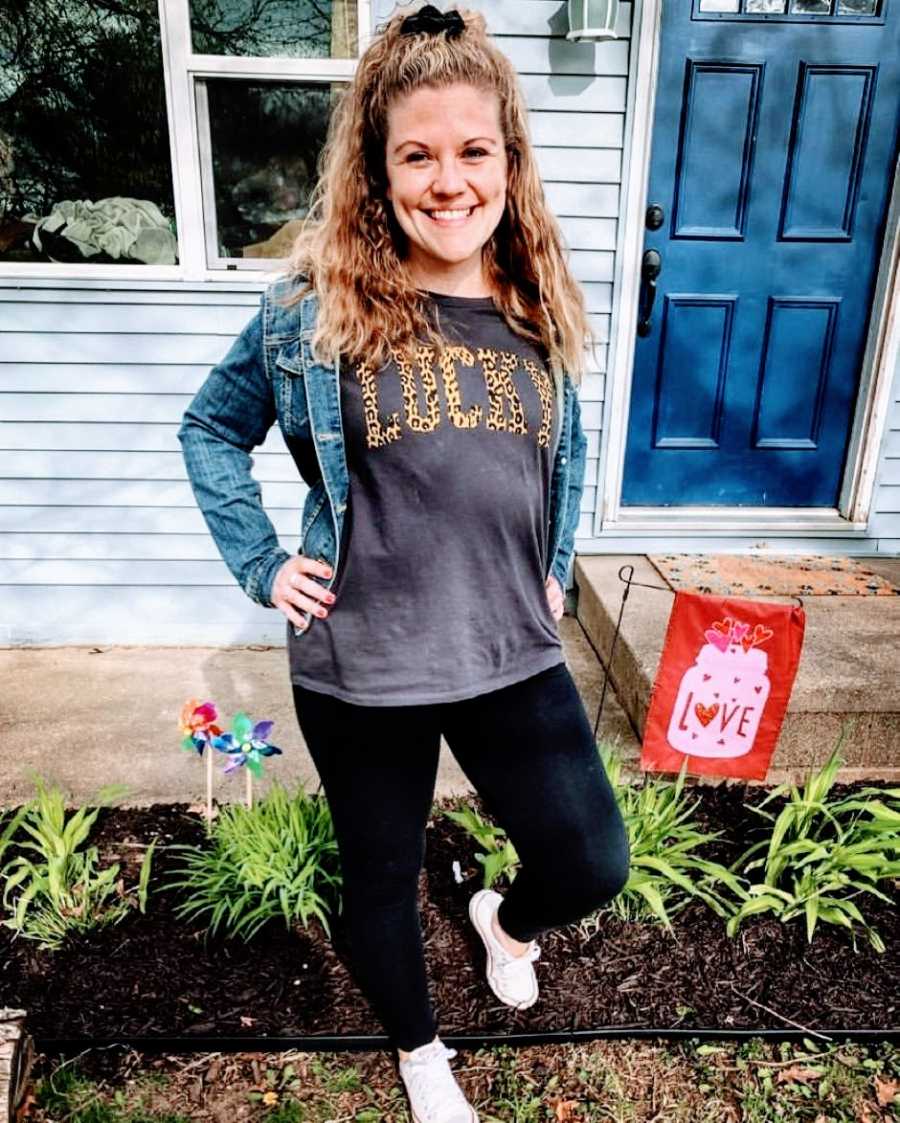 Woman takes a proud photo in front of her home with a shirt that says "lucky" in animal print on it