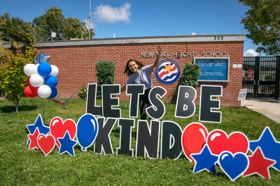 girl with let's be kind lawn sign