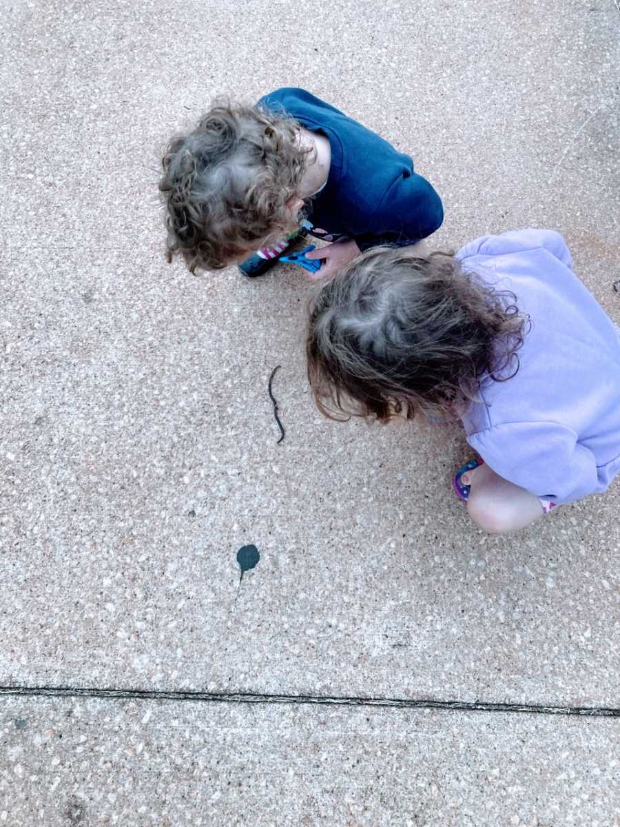 Mom snaps photo of her twins crouched down on the ground, watching a worm