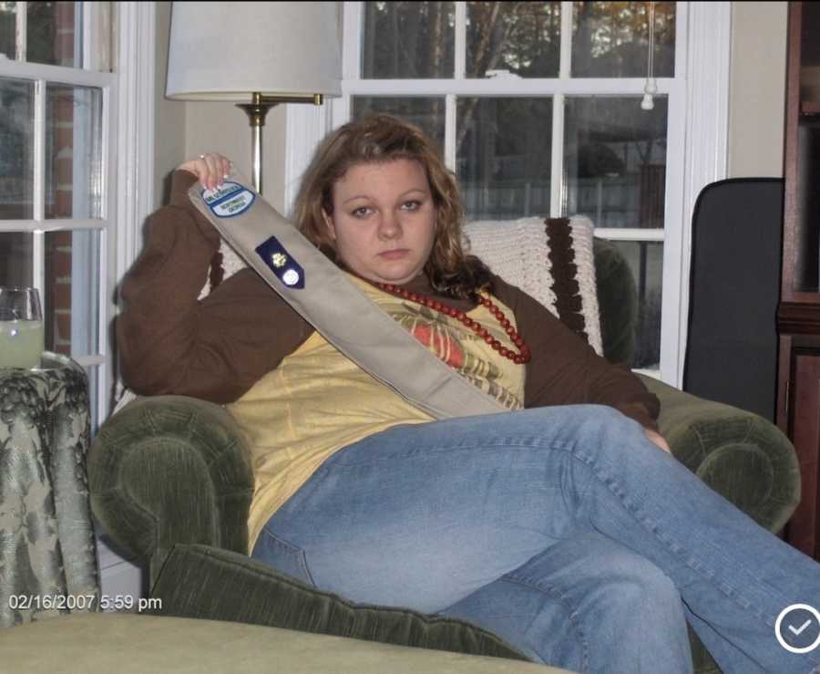 young girl sitting in chair holding sash