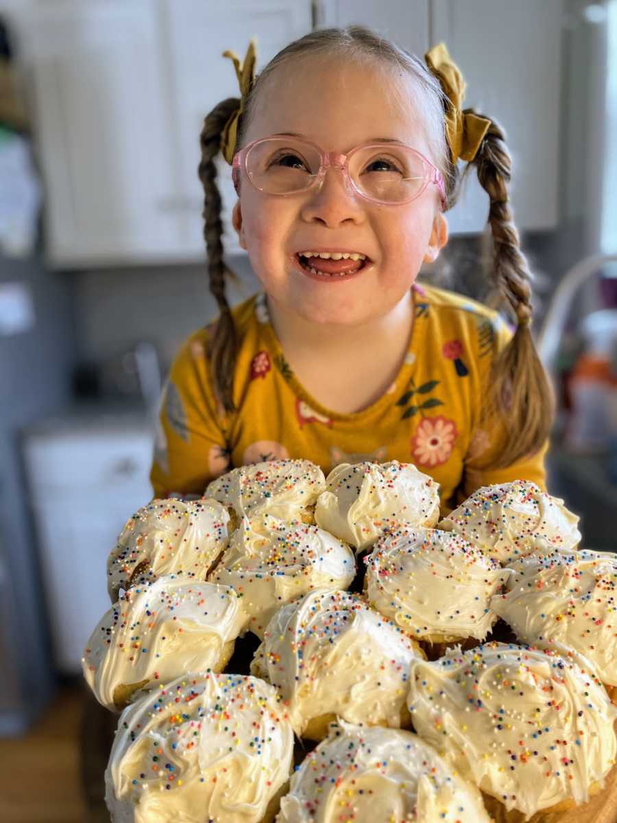 Girl with Down syndrome smiles in front a batch of freshly baked vanilla cupcakes