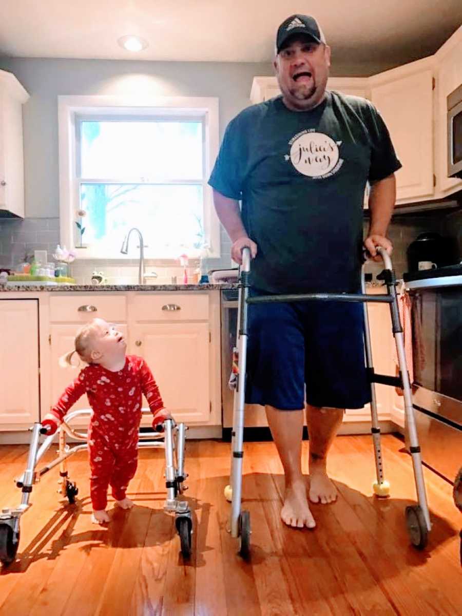 Little girl with Down syndrome practices walking with a walker with her dad's support