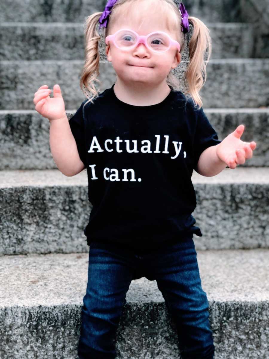 Little girl with pink glasses and purple bows in her hair wears a t-shirt that says "Actually, I can."