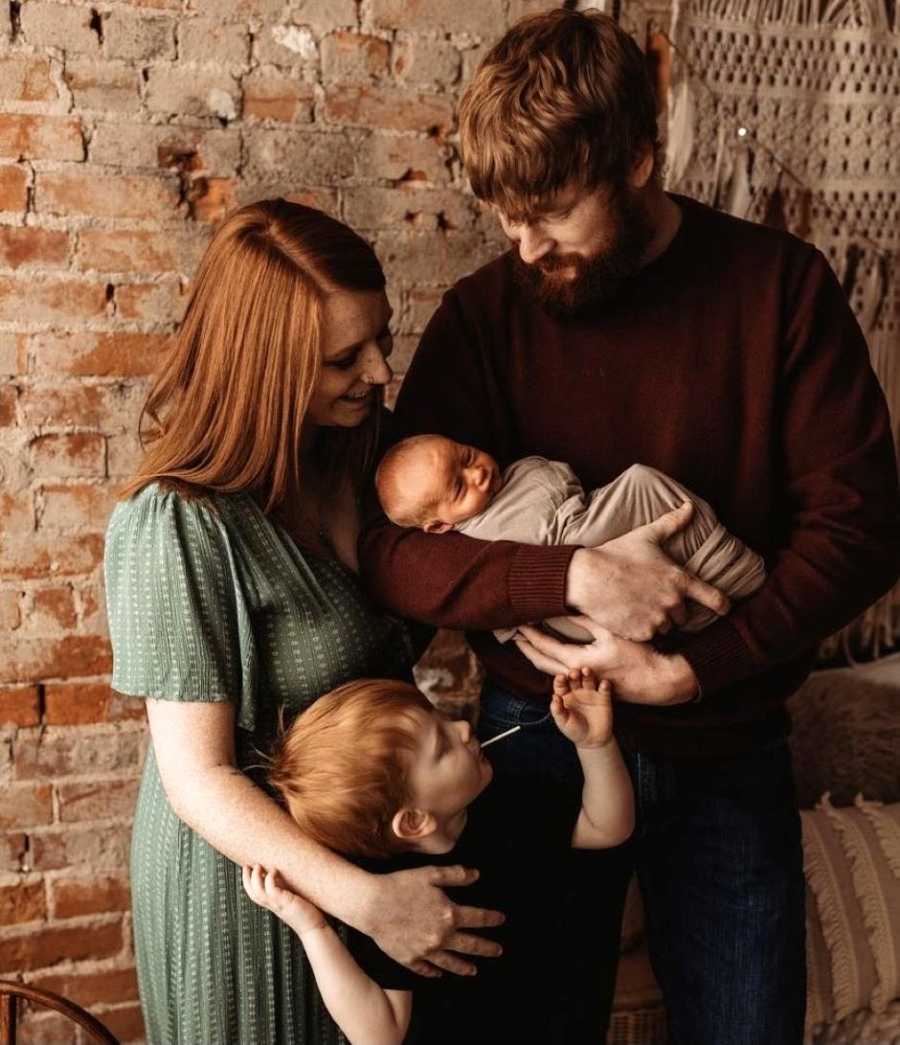 Family of four pose for a family photo together, all admiring their newborn baby boy