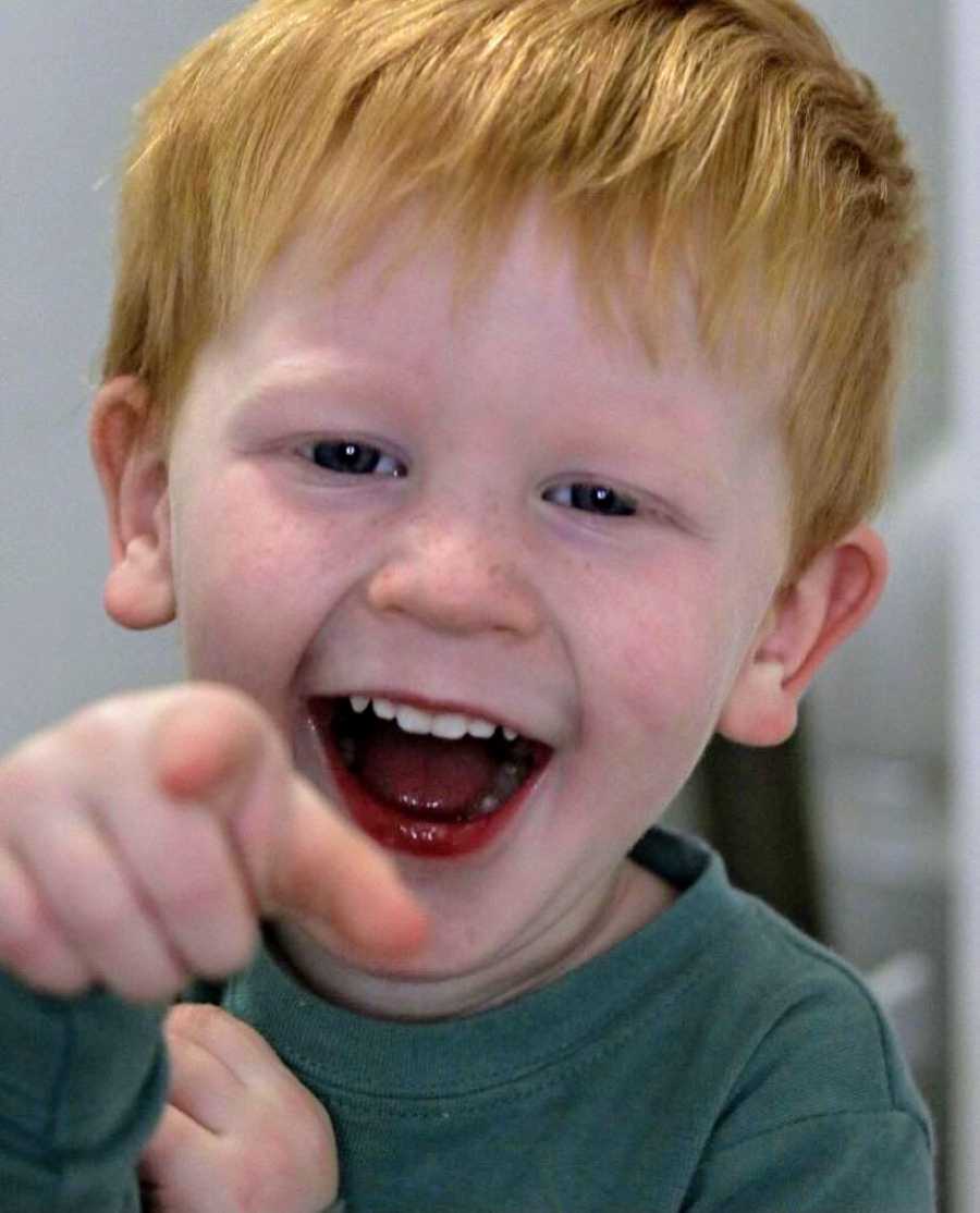 Little boy with red hair points and laughs at the camera