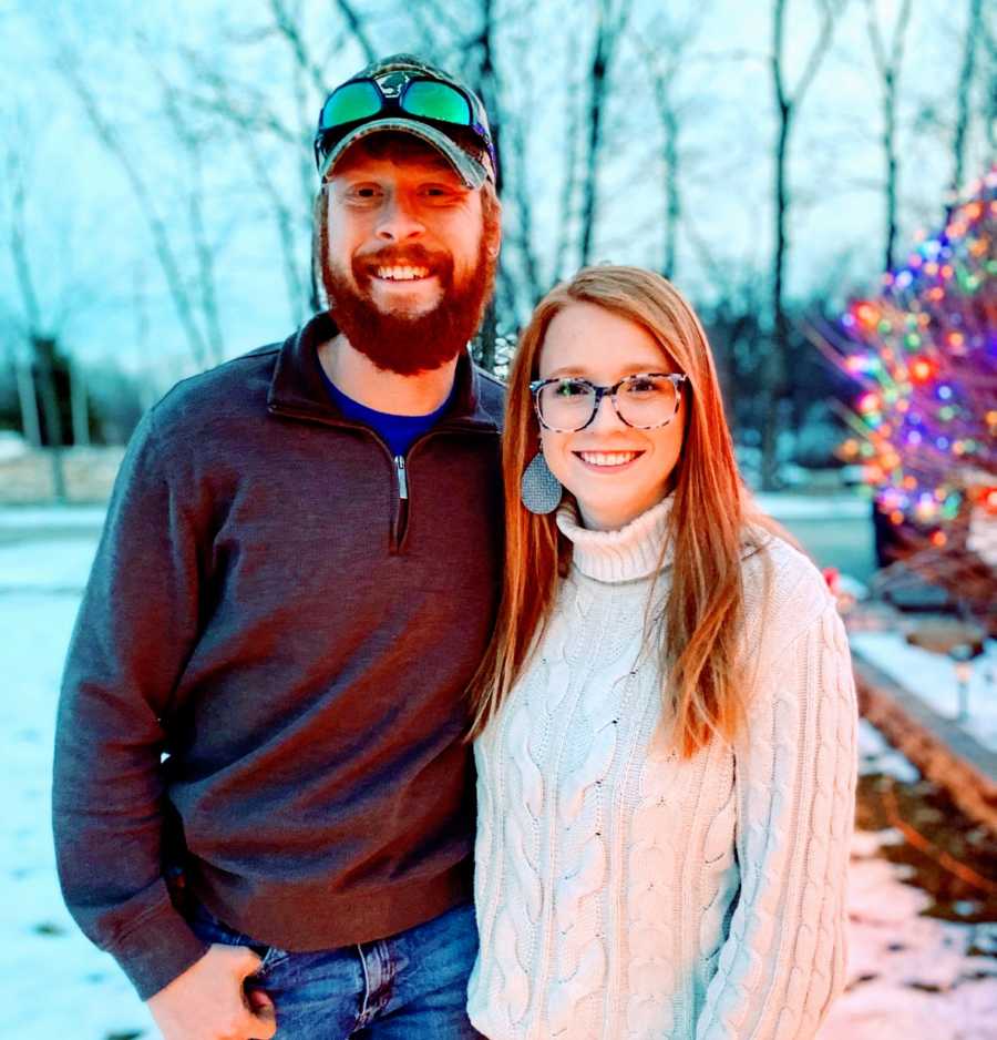 Woman with OCD takes a photo with her husband out in the snow with Christmas lights behind them