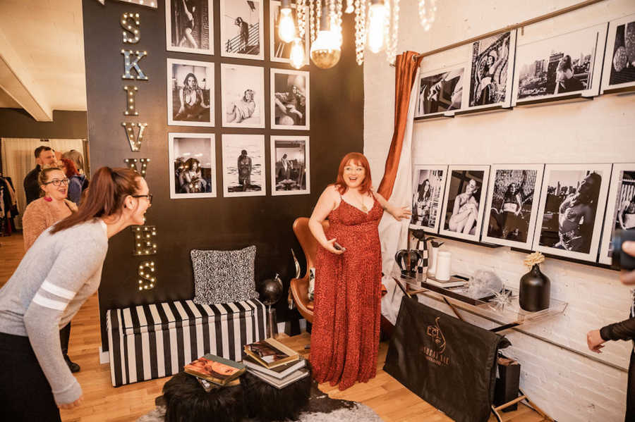 Woman wearing red dress pointing to photographs she took surrounded by friends