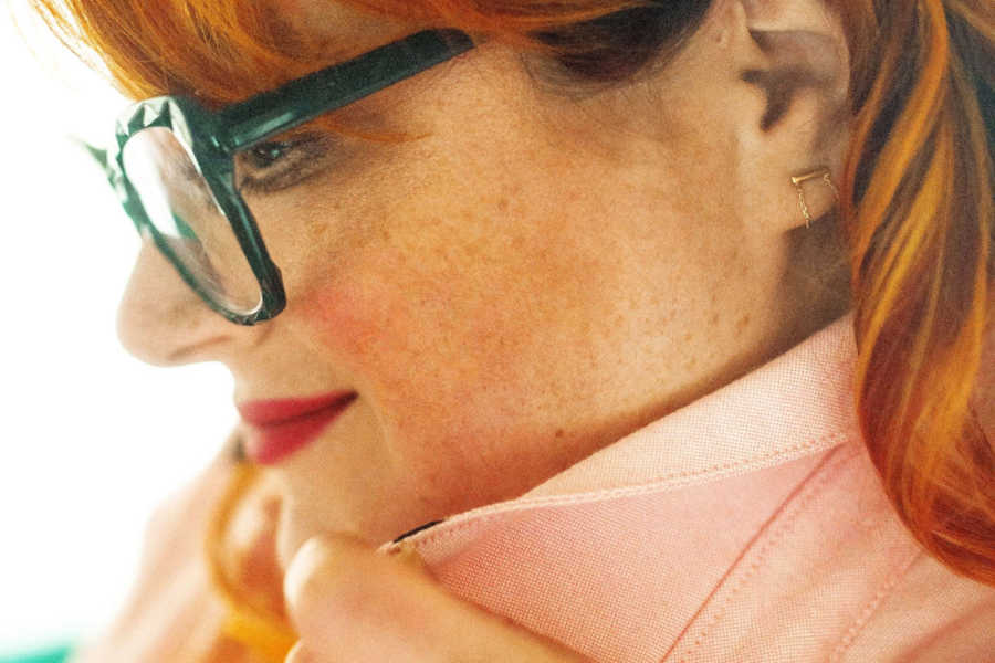 Redhead woman wearing pink shirt and green glasses looking off into distance