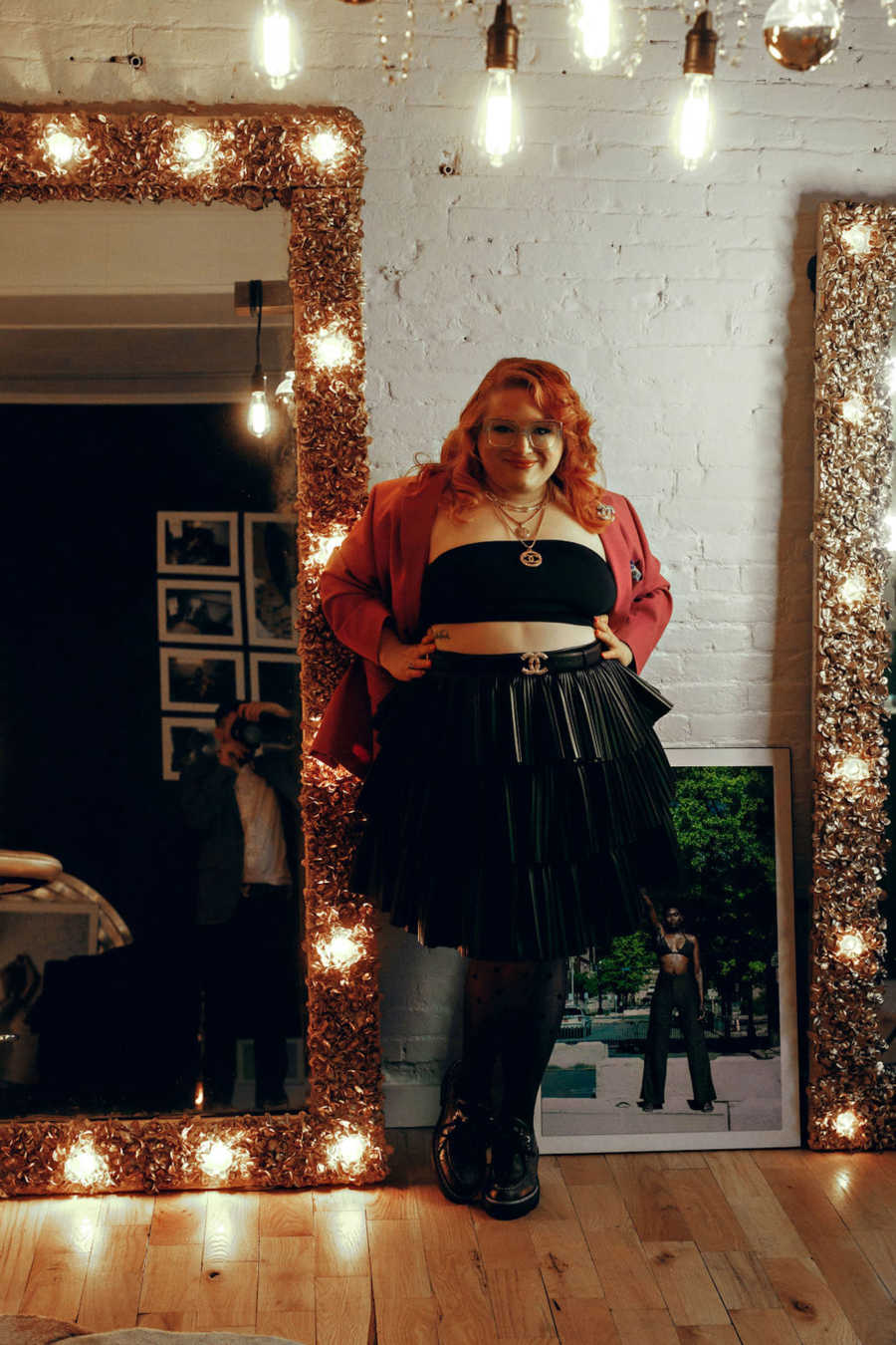 Woman wearing black crop top and skirt with hands on hips smiling in front of mirror and lights