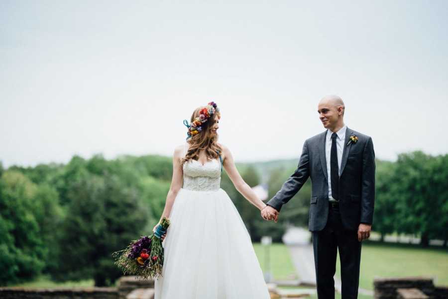 Newly weds smile at each other while they hold hands in their wedding day outfits