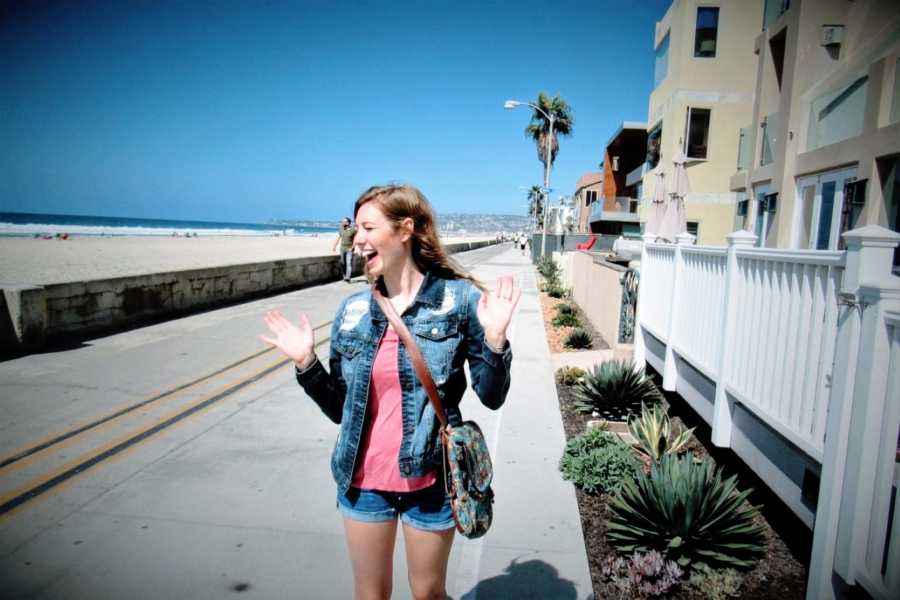 Woman celebrates being out at the beach by throwing her hands into the air and smiling