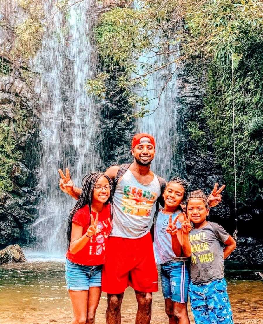 Single black dad takes three kids on a hike and pose for a photo in front of a waterfall