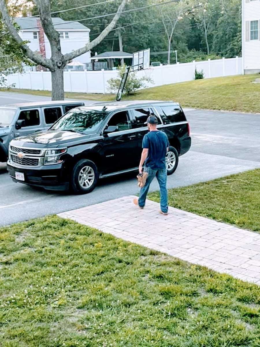 Man walks towards his car while heading off to work, carrying work boots