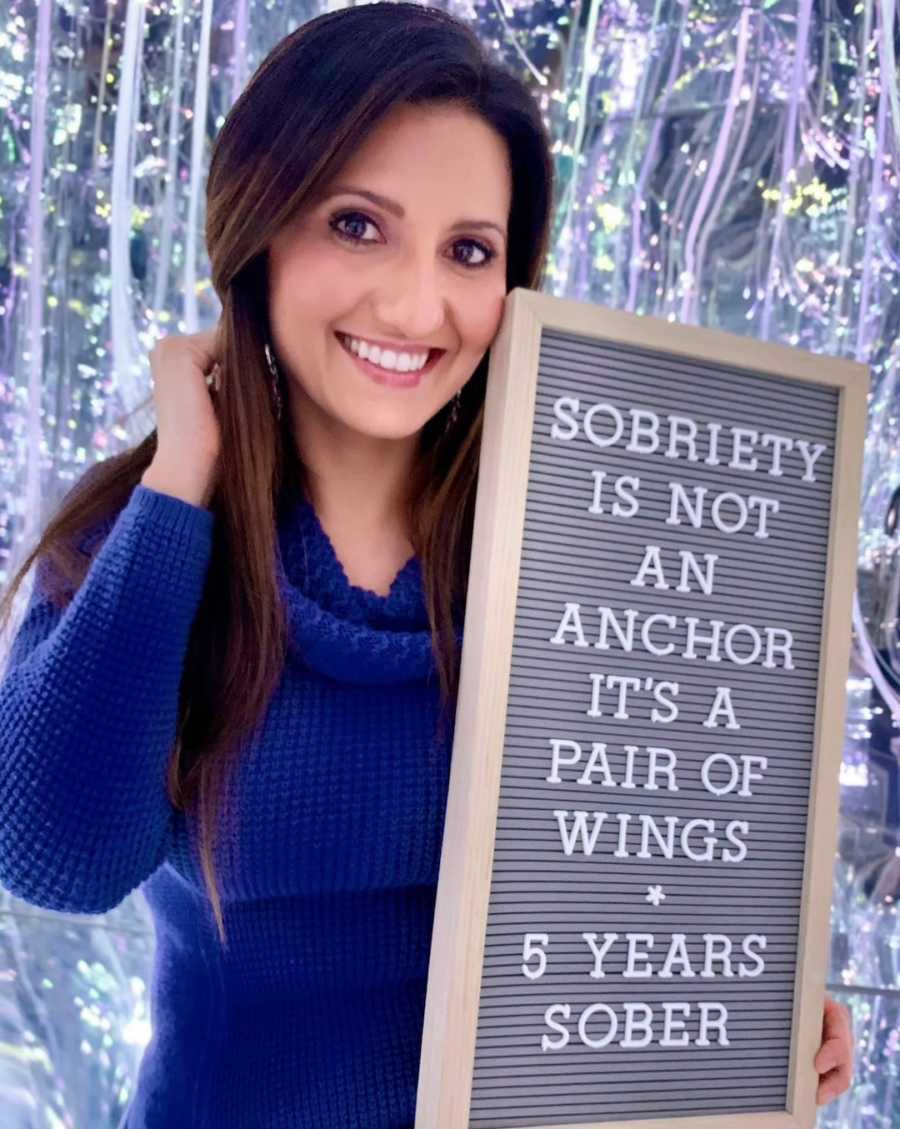 woman holding "five years sober" sign- sobriety is not an anchor it's a pair of wings