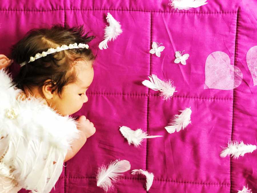 Mom snaps photo of newborn daughter laying on a pink blanket while dressed up as angel