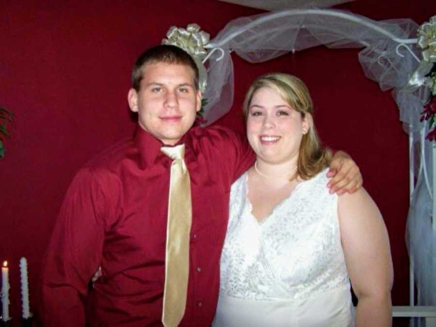 Couple take a photo together on their wedding day, groom in a red shirt and gold tie, bride in a size 24 white dress