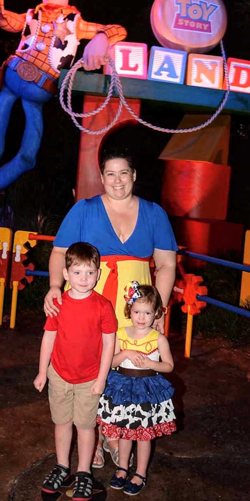 Mom takes a photo with two of her kids in Toy Story Land in Disney while her daughter is dressed up like Jessie