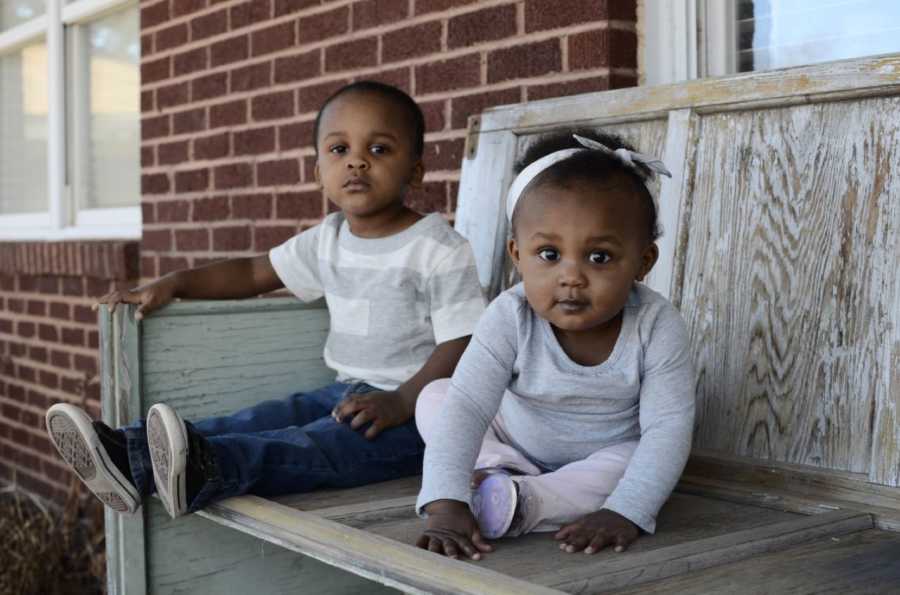 Young siblings sit on a wooden bench and stare into the camera during a photoshoot