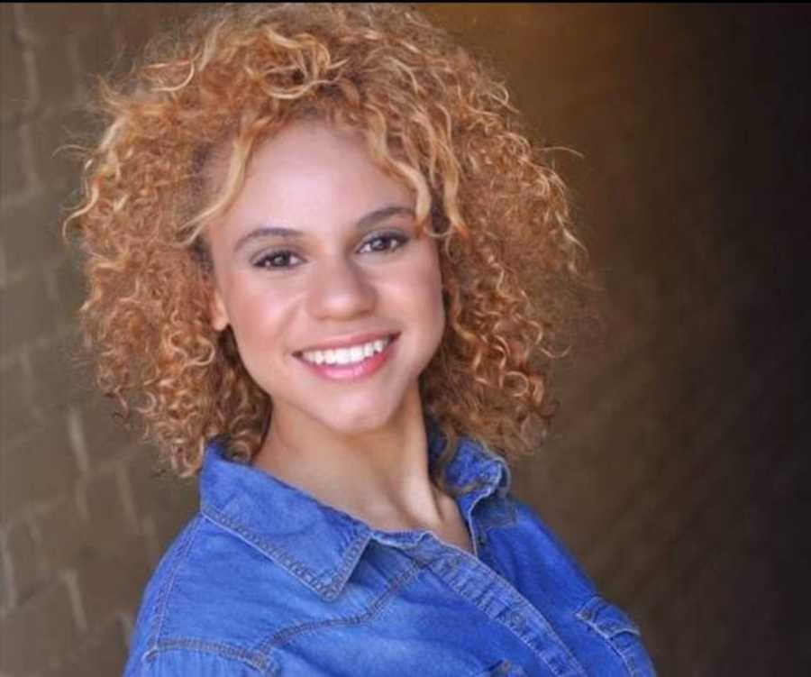 woman in blue shirt with curly brown hair smiling