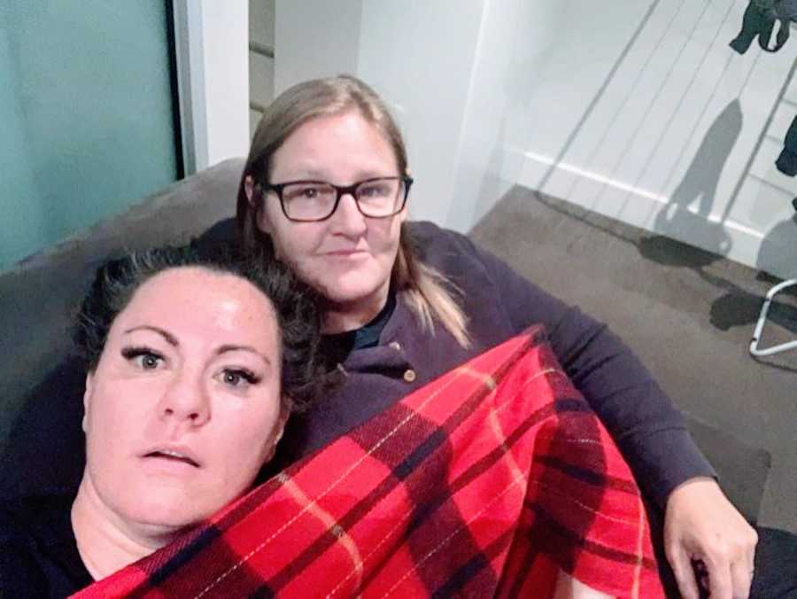 Couple cuddle on the couch under a red and black plaid fuzzy blanket