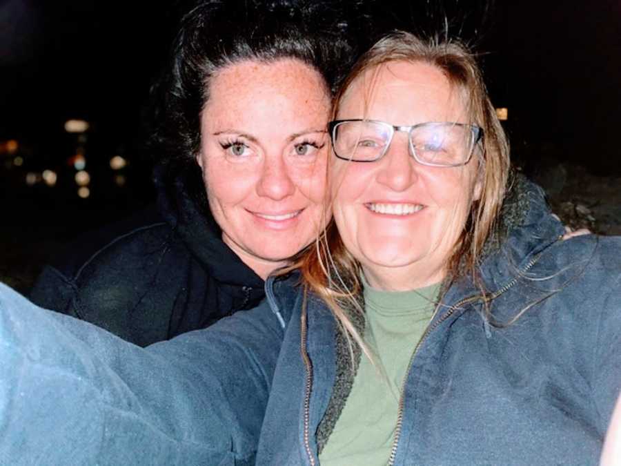 Lesbian couple take a selfie in the dark with the city lights behind them