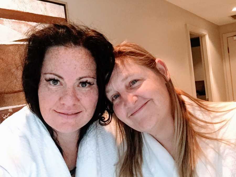 Lesbian couple in matching white, fluffy robes take a selfie while enjoying a romantic evening in a hotel