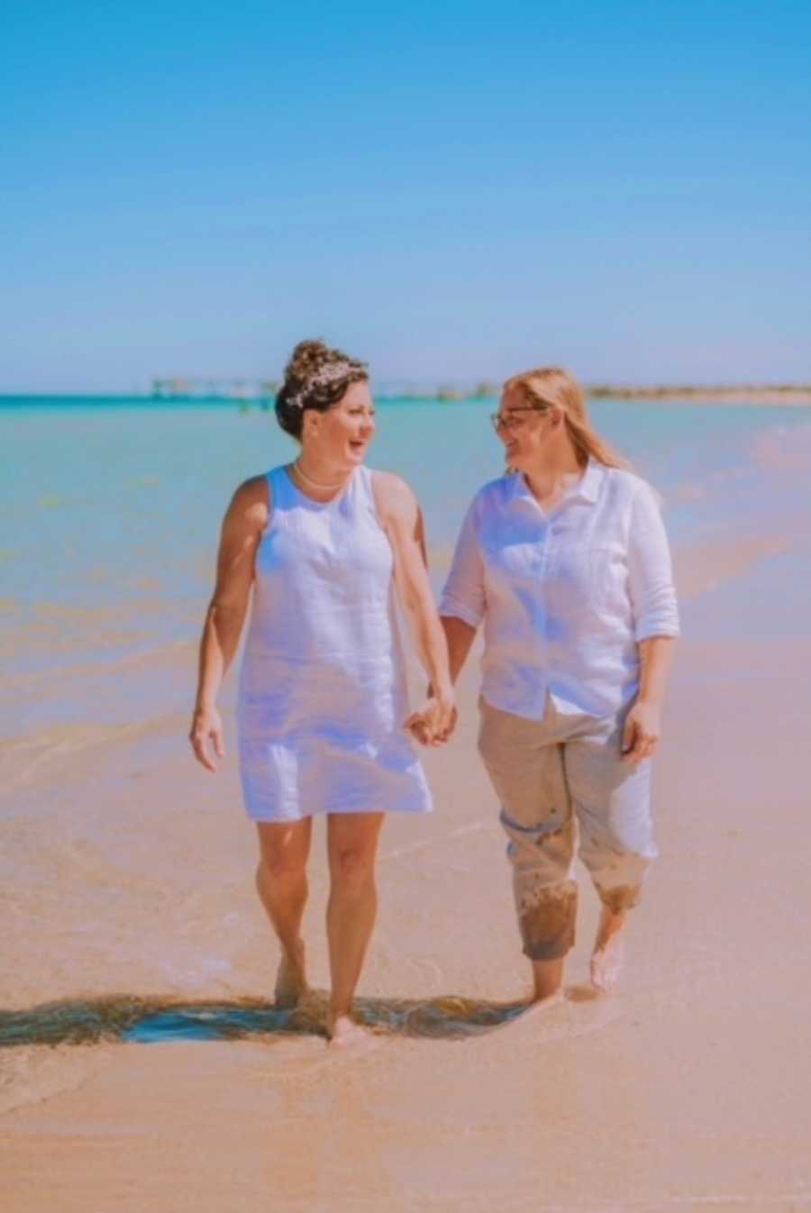 Couple walk hand-in-hand down the beach after their wedding, celebrating their love