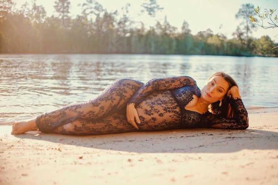 pregnant woman laying by lake, holding stomach