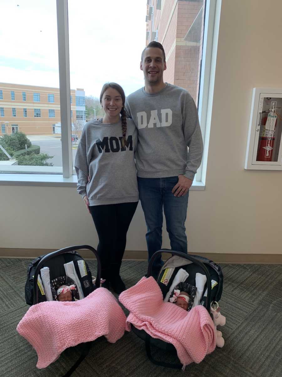 twins in matching carriers, with mom and dad