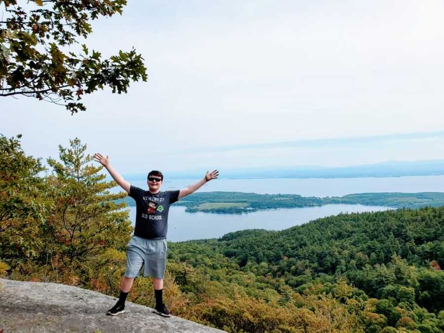 Photo of young boy celebrating the marvelous waterfront view during a hike