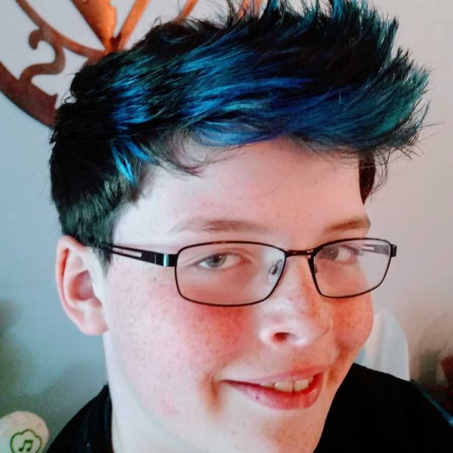 Young boy with spiky blue hair and glasses takes a selfie