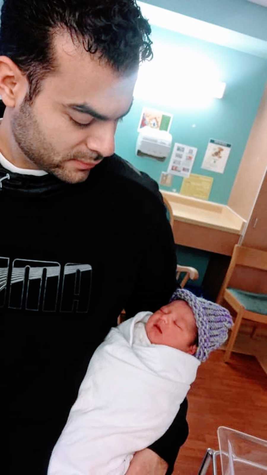 Dad looks down at his newborn while he holds him in the hospital