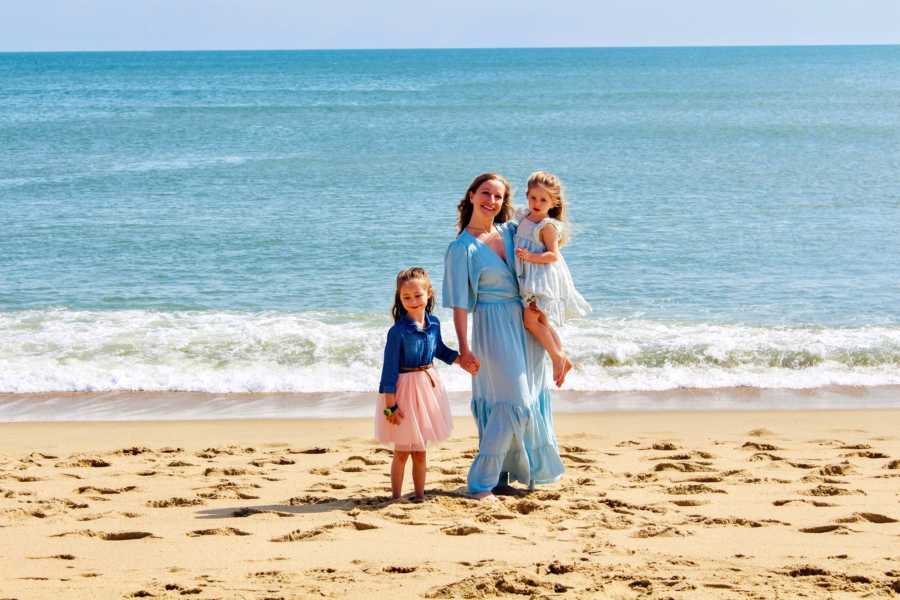 Girl mom takes a beautiful beach photo with her two daughters, all wearing flowy dresses blowing in the wind