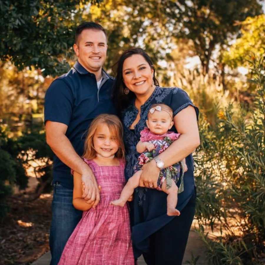 Family of four take beautiful outside photo, the parents in blue denim and their daughters in pink dresses