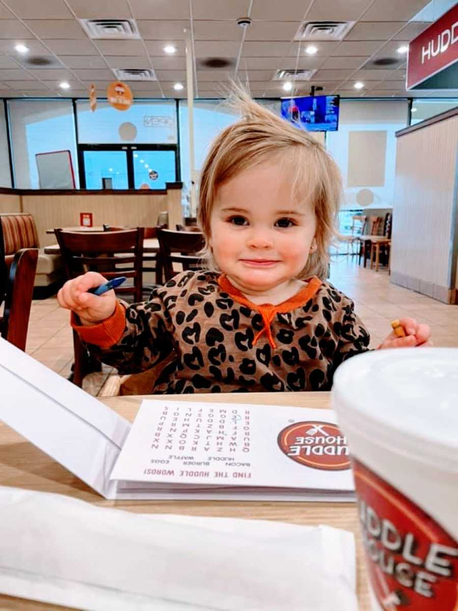 Little girl with heart-patterned shirt sits down at the Huddle House and colors