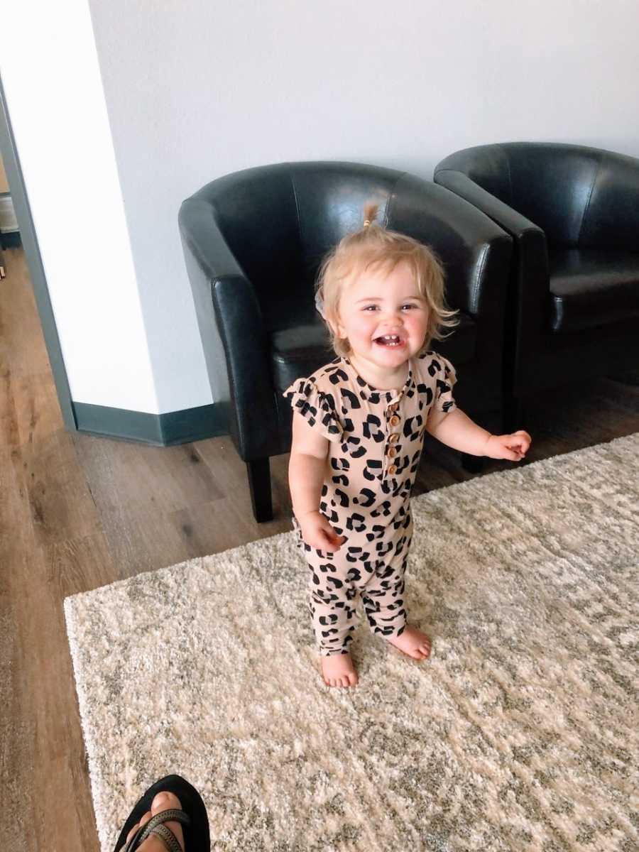 Little girl in patterned romper smiles while walking around the living room