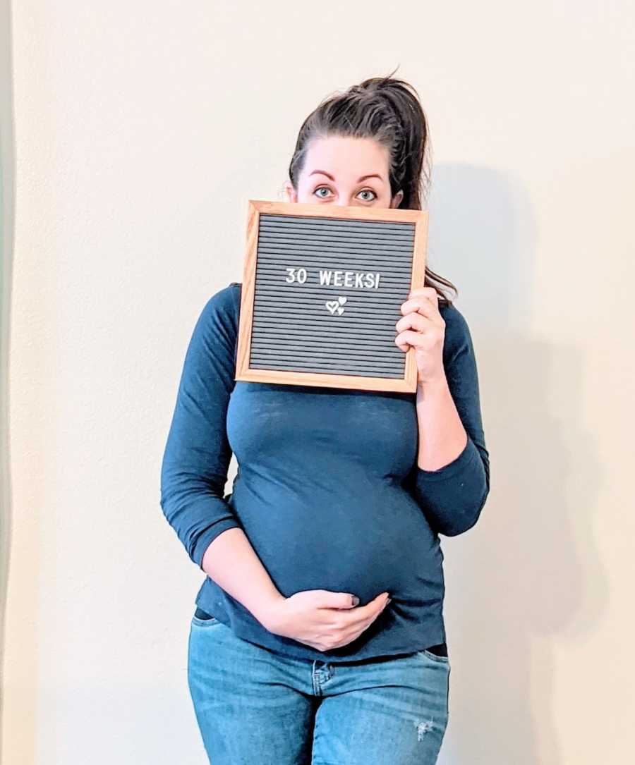 Pregnant woman holding up letter board in front of face 