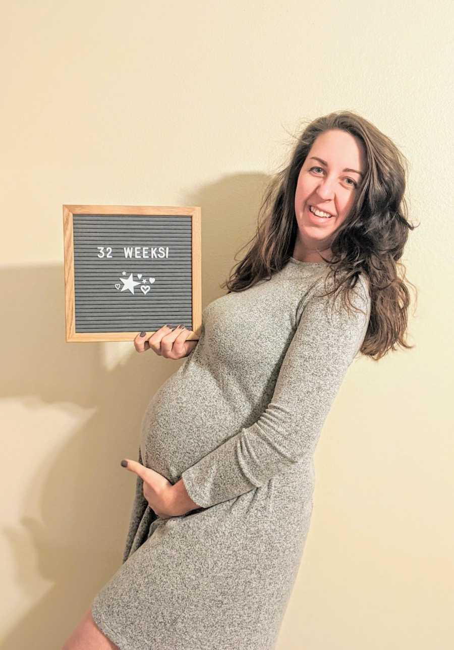 Pregnant woman holding up letter board and smiling