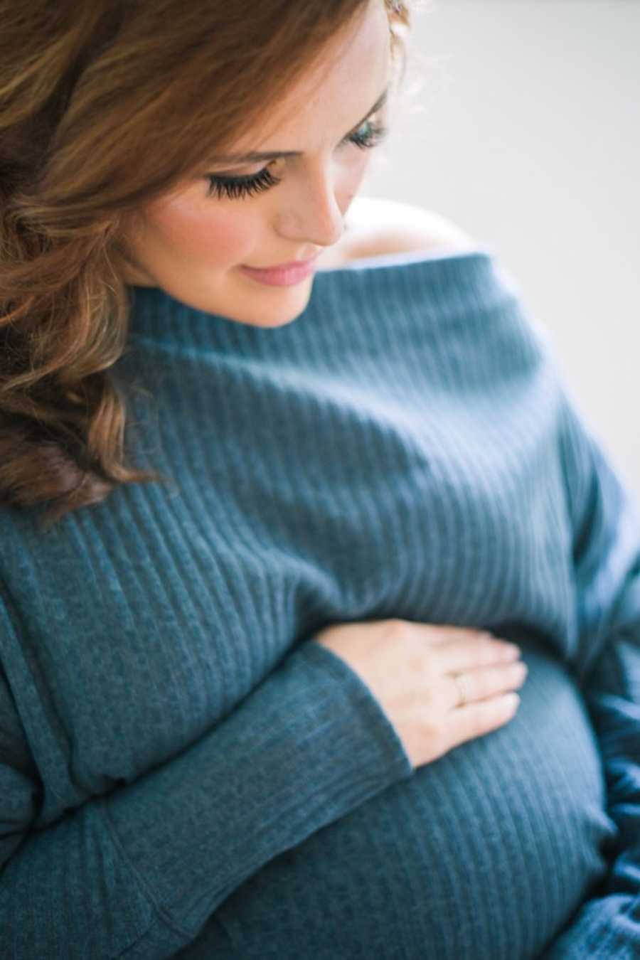 Pregnant woman wearing blue sweater with hands on belly