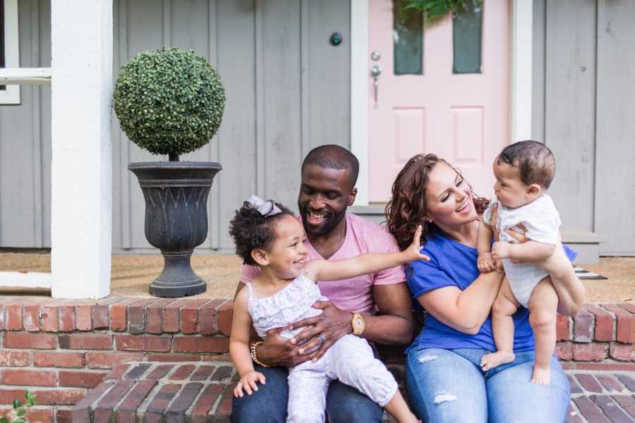 Family of four sitting on front steps of house laughing and smiling